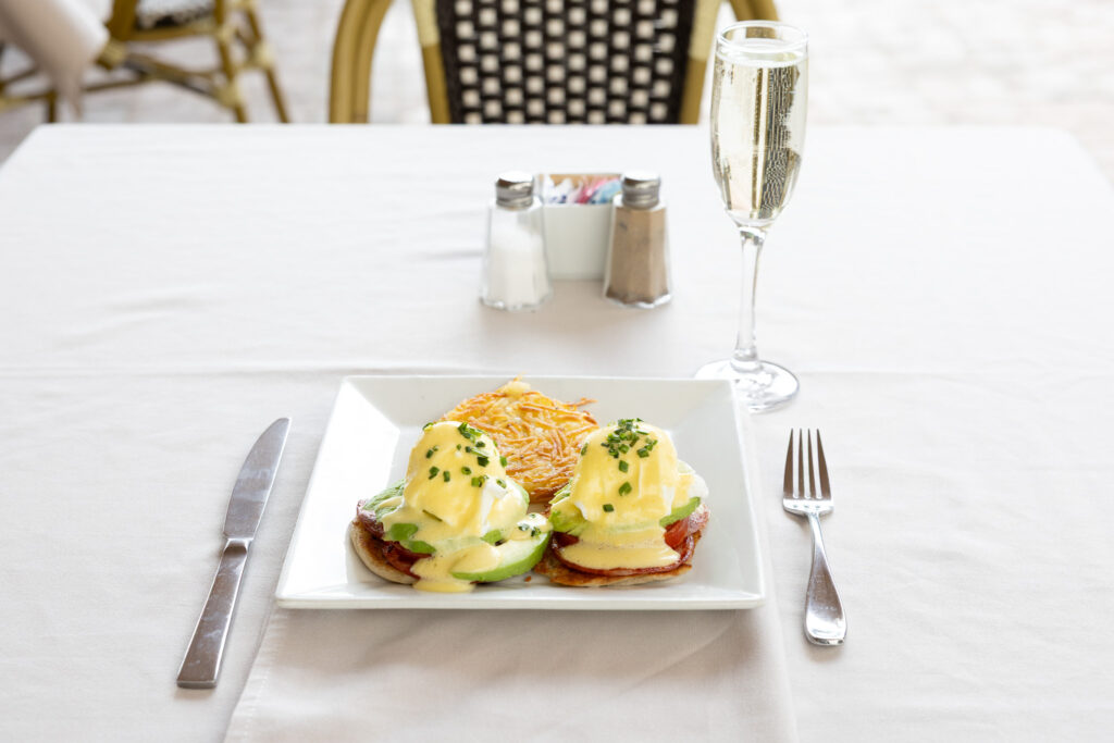 Egg Benedict on a table setting with a knife and fork next to the plate with Moscato